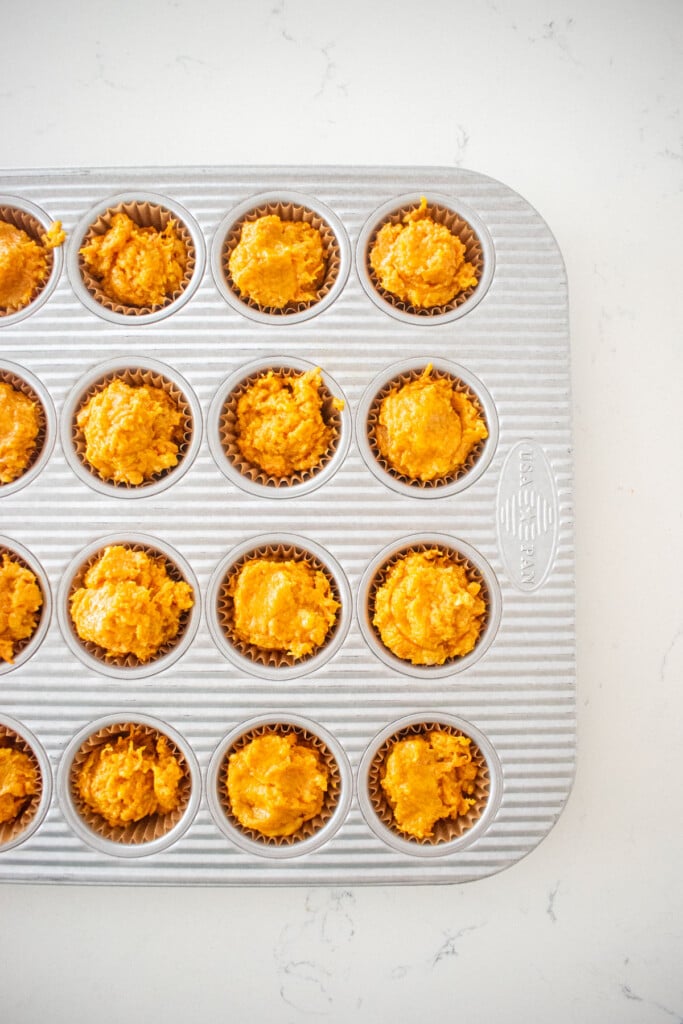 healthy dog muffins batter scooped into a mini muffin pan on a white marble counter.