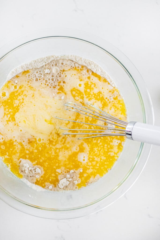 ingredients for homemade buttermilk pancakes in a glass mixing bowl with a whisk on a white marble counter.