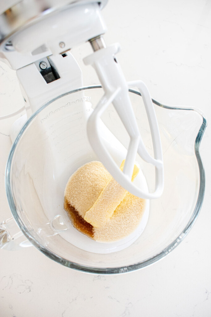 butter sugar and vanilla in a glass mixing bowl on a white marble counter.