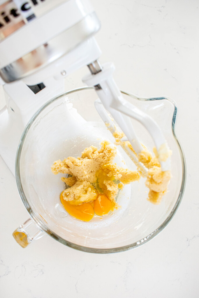 creamed butter and sugar in a glass mixing bowl with eggs on a white marble counter.