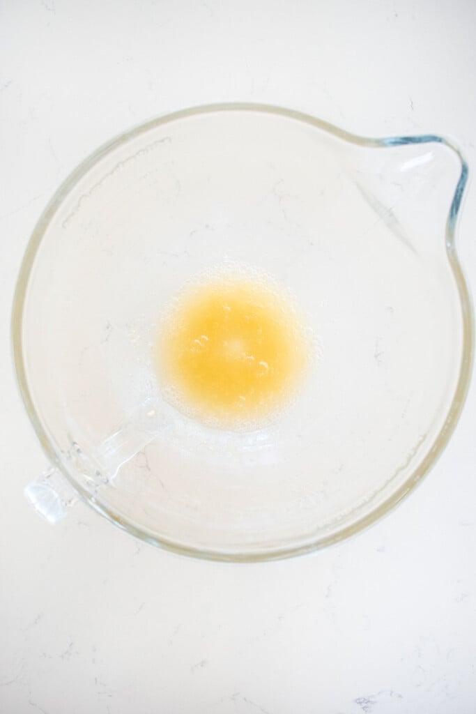 gelatin and water in a glass mixing bowl on a marble countertop.