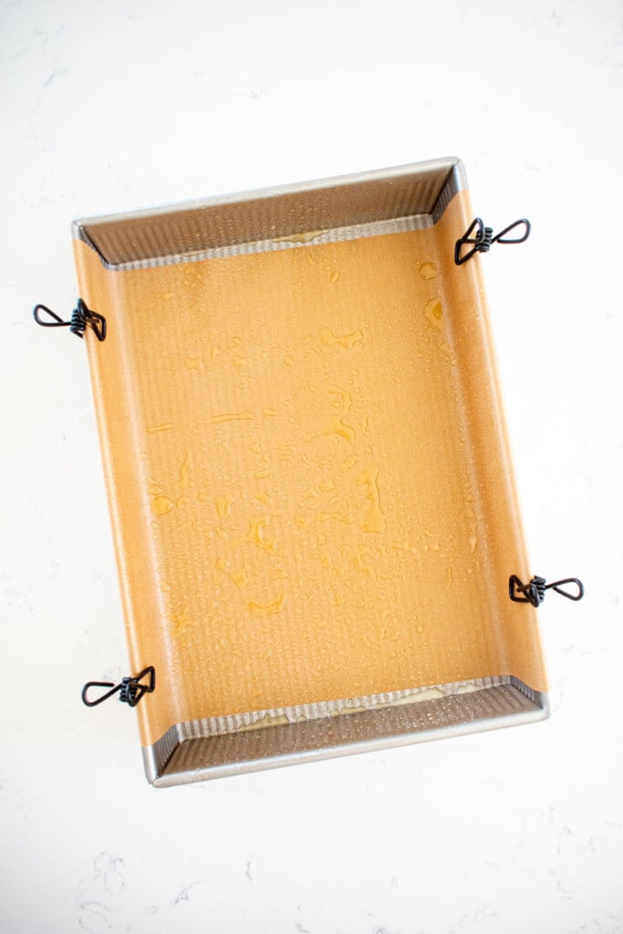 greased baking pan with parchment paper on a marble countertop.