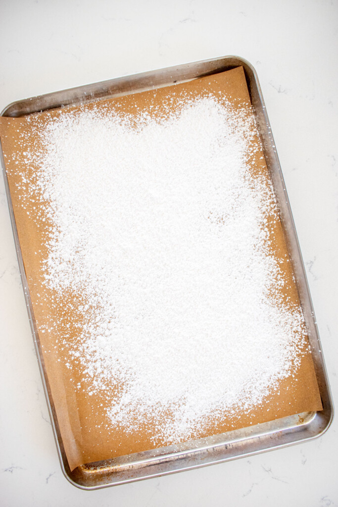 baking sheet with parchment paper and powdered sugar on a marble countertop.