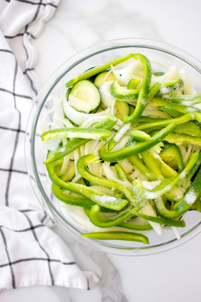 refrigerator pickles in a glass mixing bowl on a white marble countertop.
