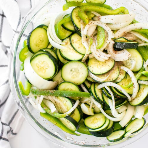 refrigerator pickles in a glass mixing bowl on a white marble countertop.