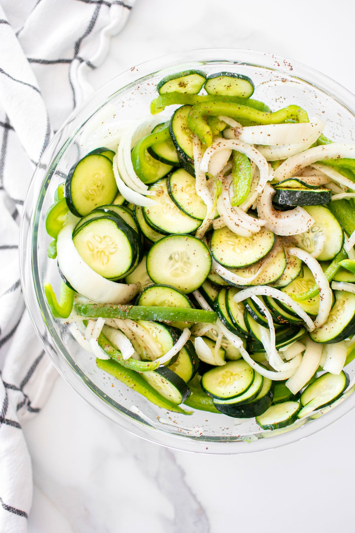refrigerator pickles in a glass mixing bowl on a white marble countertop.