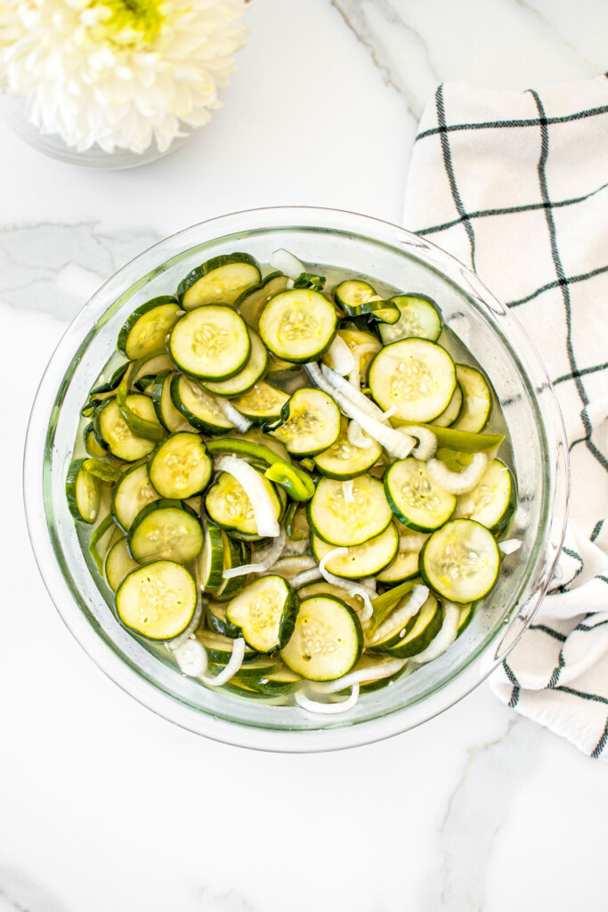 refrigerator pickles in a glass mixing bowl on a white marble countertop.