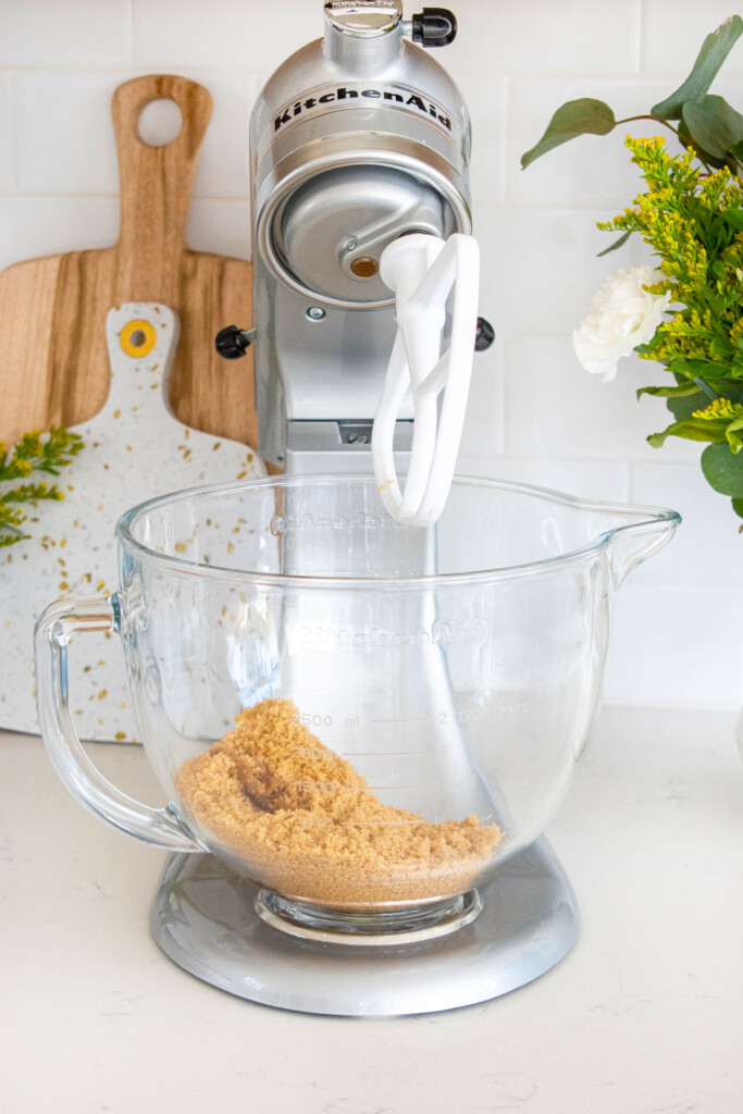 butter and brown sugar in a glass mixing bowl on a white marble counter.
