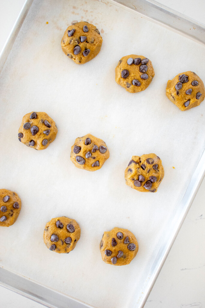 rye chocolate chip cookie dough balls on a baking sheet on a white marble counter.