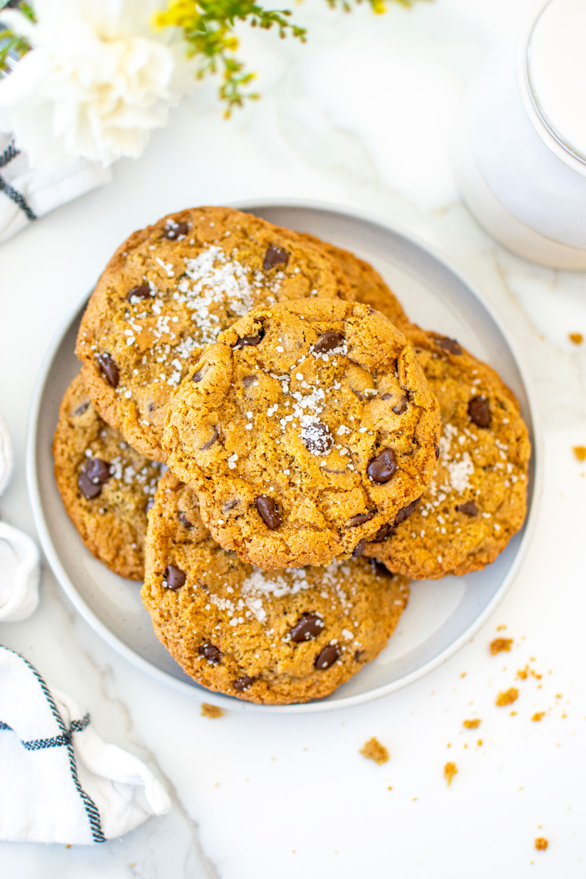 plate of rye chocolate chip cookies with flaky sea salt on a plate on a white marble counter.