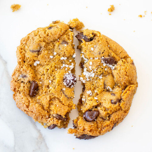 rye chocolate chip cookie with flaky sea salt broke in half on a white marble counter.