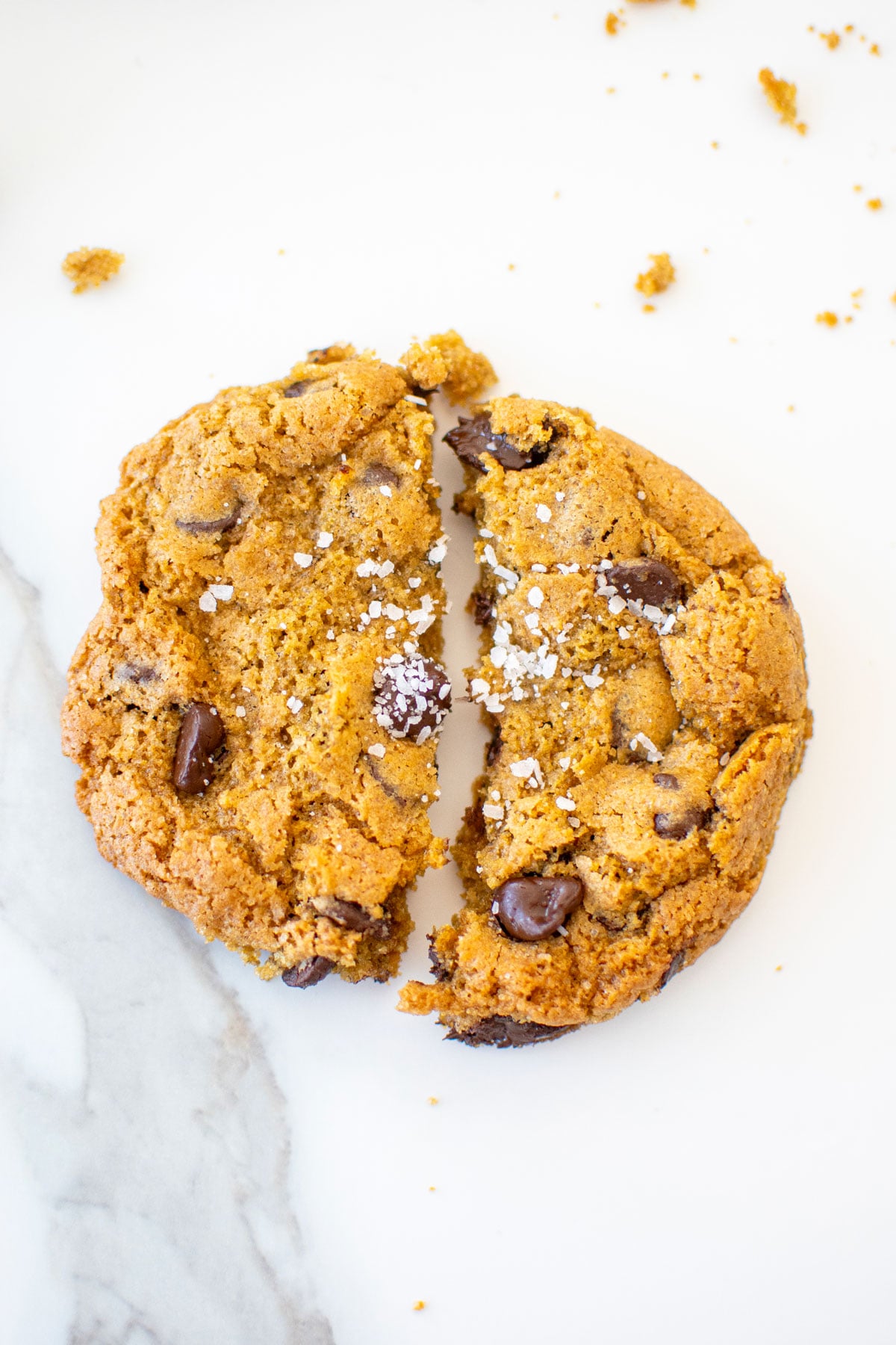 rye chocolate chip cookie with flaky sea salt broke in half on a white marble counter.
