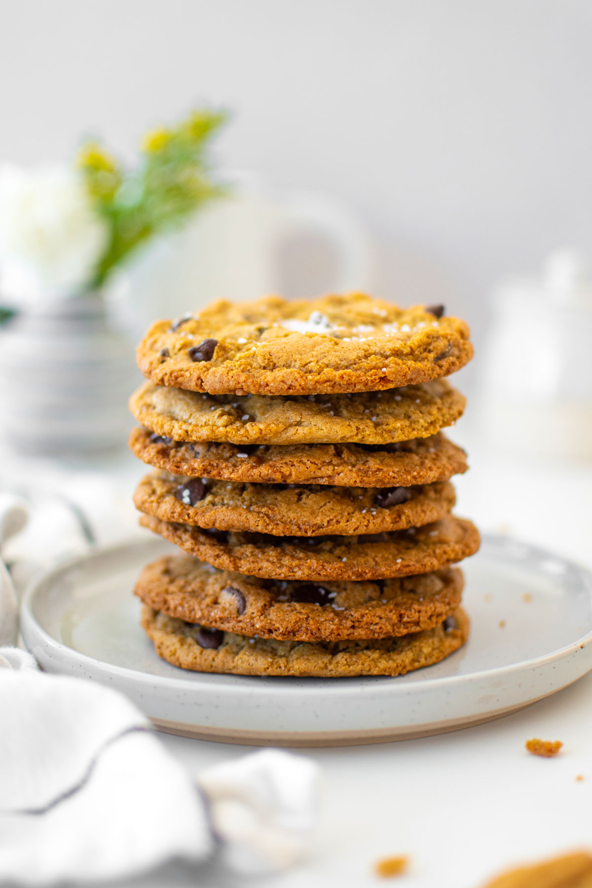 stack of rye chocolate chip cookies with sea salt on a plate on a white marble counter with fresh flowers.