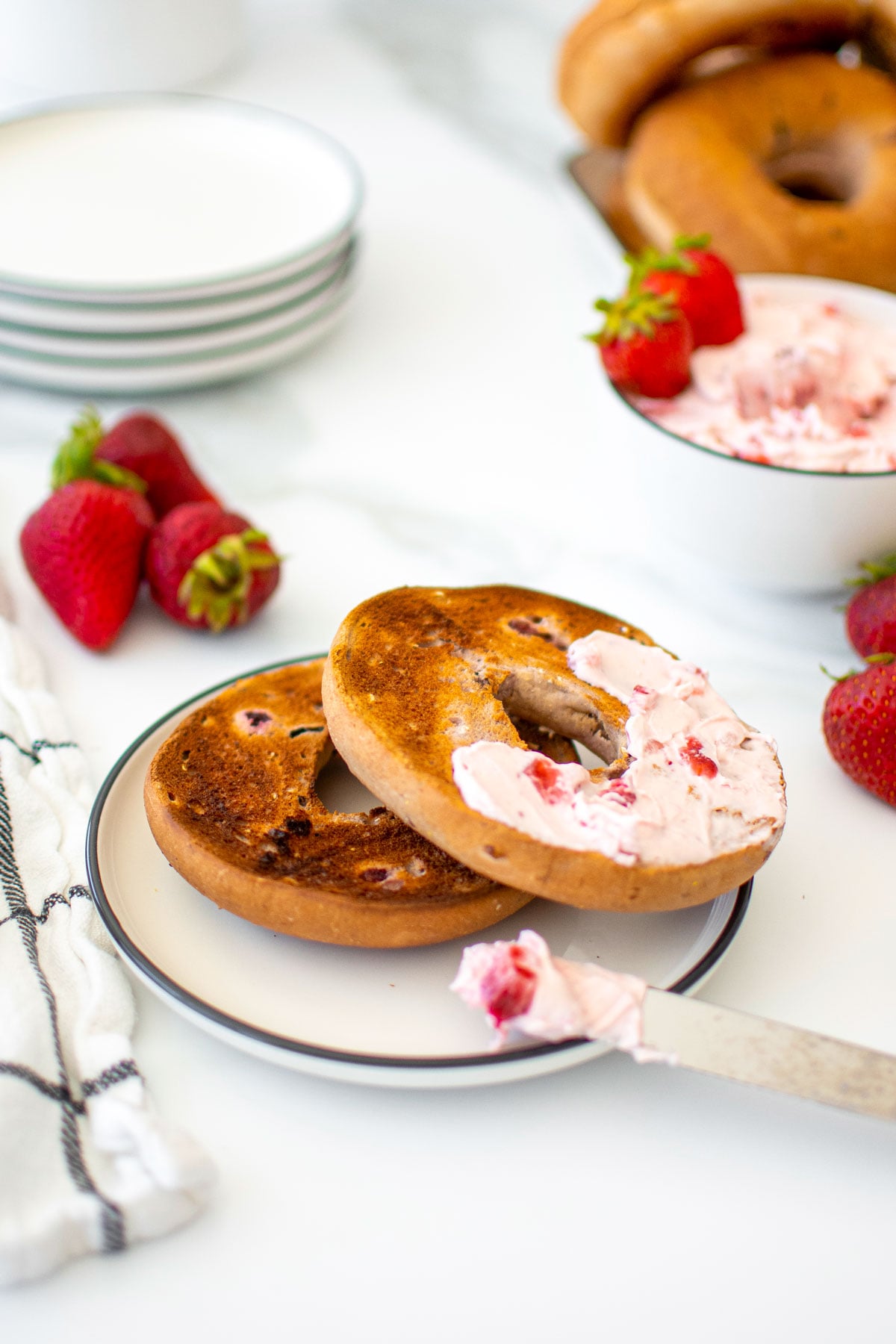 bagel with strawberry cream cheese spread on a white plate on a marble counter.
