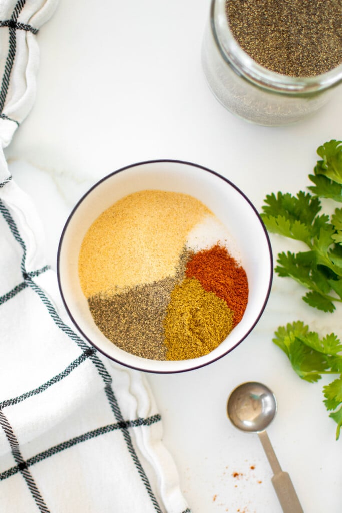 organic homemade taco seasoning ingreidnet in a bowl on a marble counter with cilantro.