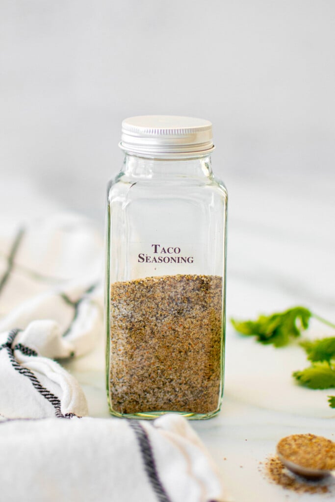 organic homemade taco seasoning in a spice jar on a marble counter with cilantro.