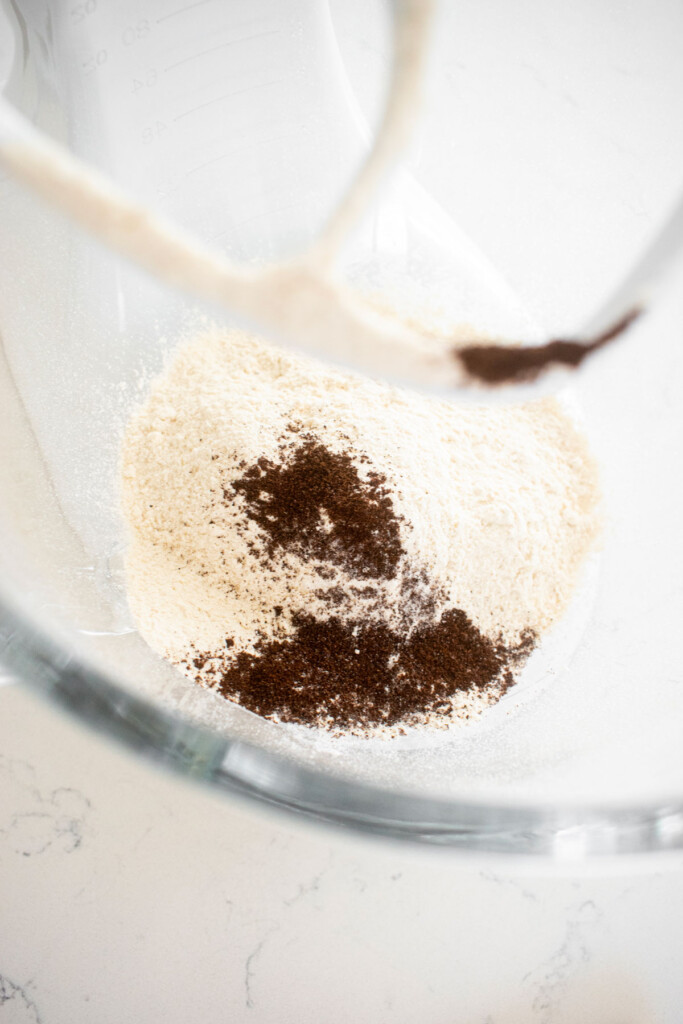flour sugar and ground vanilla bean in a glass mixing bowl on a white marble counter.