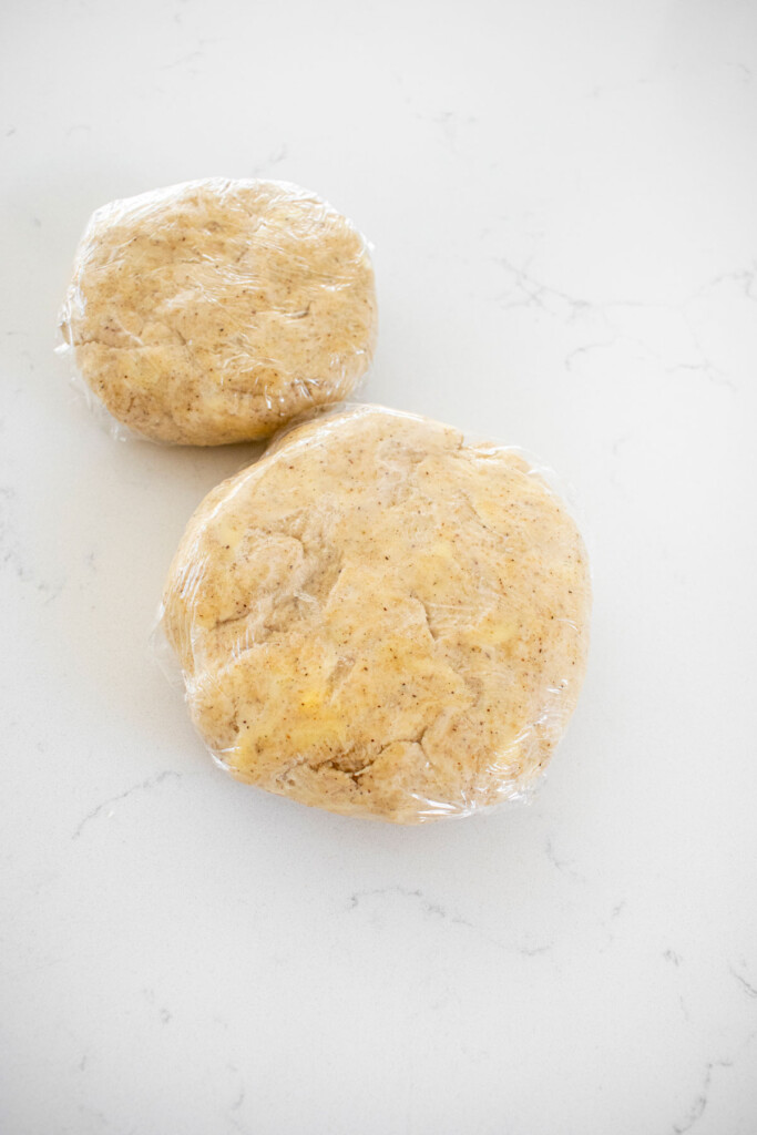 vanilla bean pie crust disks wrapped in plastic wrap on a white marble counter.