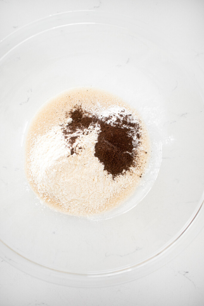 vanilla bean apple pie filling ingredients in a glass mixing bowl on a white marble counter.