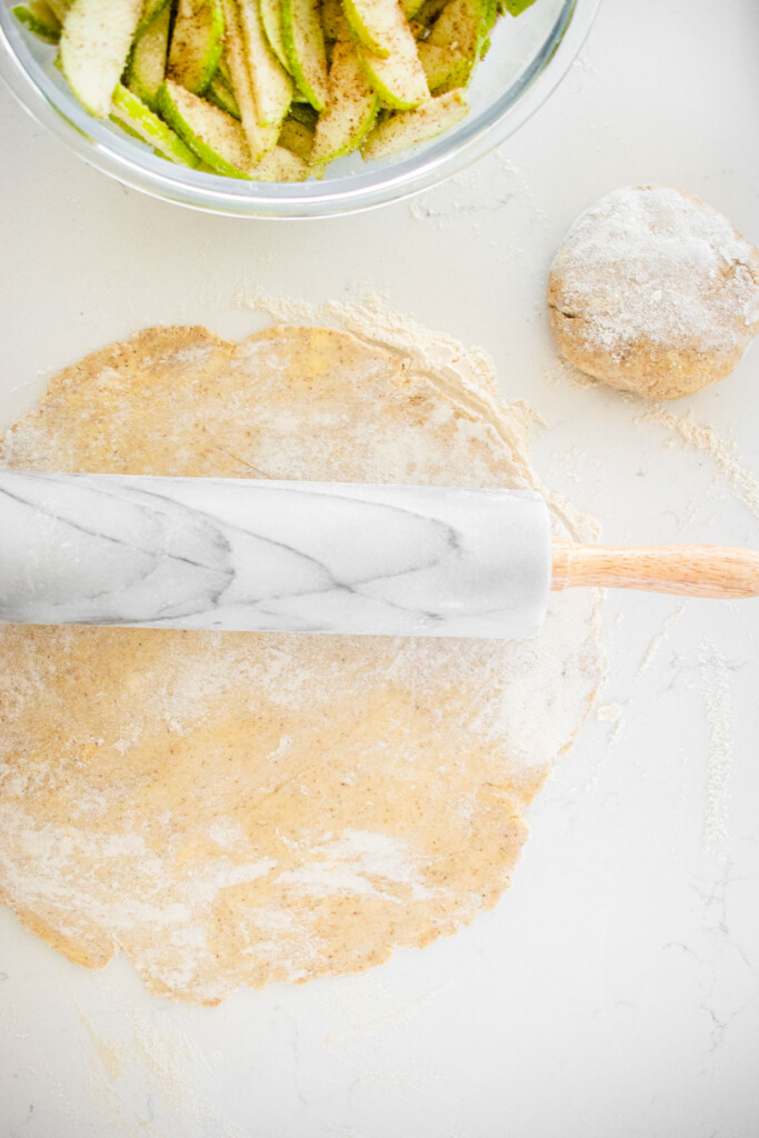 vanilla bean pie crust being rolled out with a marble rolling pin on a white marble counter.