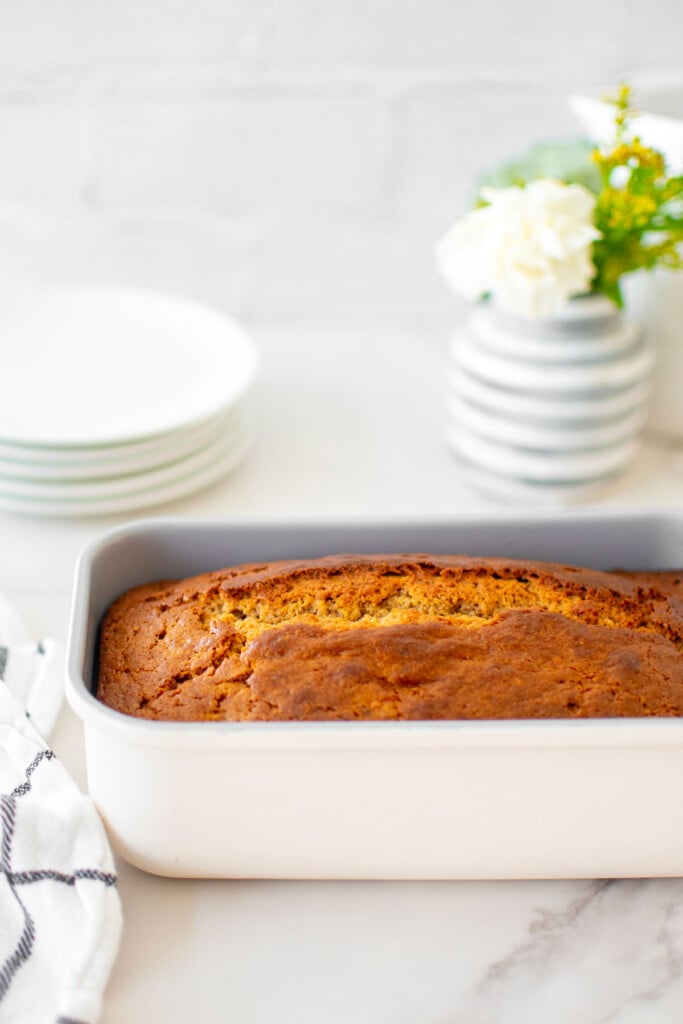 almond butter banana bread in a cream loaf pan on a white marble counter.