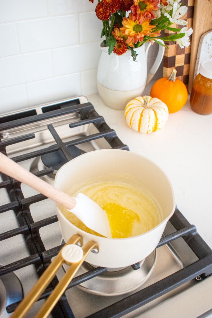 small saucepan with melted butter being stirred over the stovetop with pumpkin on a counter.