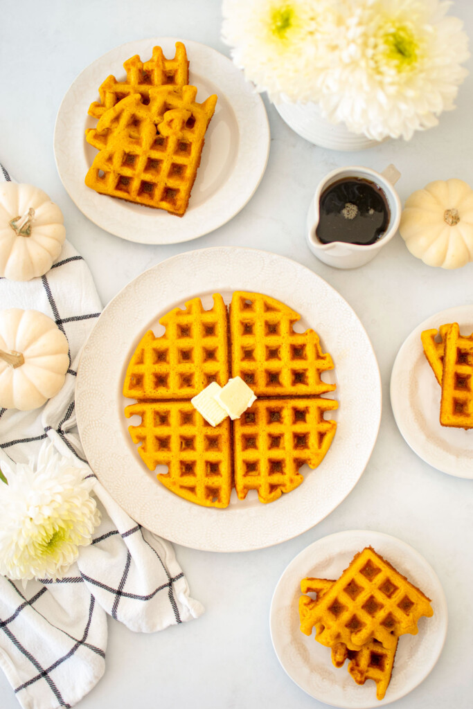 buttermilk pumpkin waffles on a white plate with butter on a white table with fresh flowers and maple syrup.