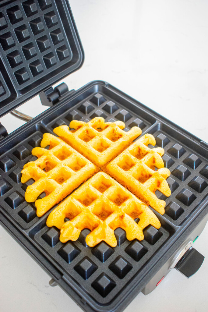 buttermilk pumpkin waffle in a waffle iron on a marble counter.