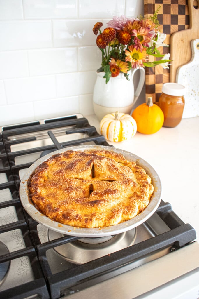golden brown caramel apple pie cooling on top of an oven.