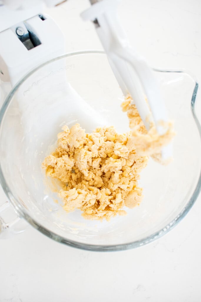pie dough in a glass bowl of a stand mixer on a marble counter.