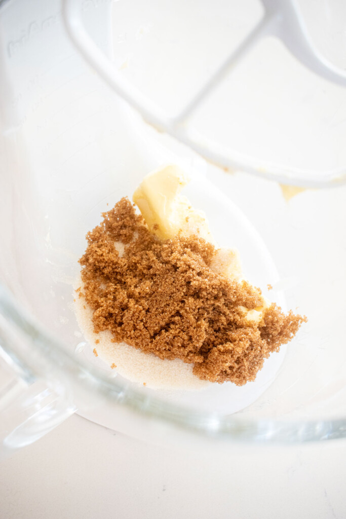 sugar and butter in a glass mixing bowl on a white marble counter.