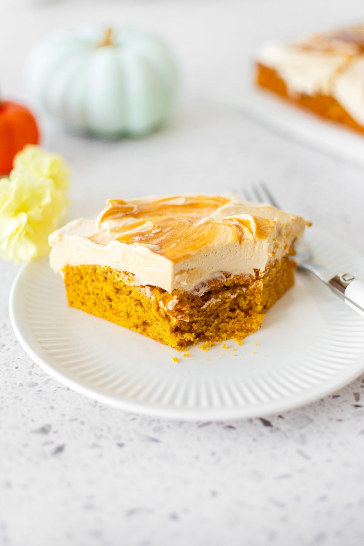caramel pumpkin spice snack cake slice on a white plate on a stone counter with pumpkins.