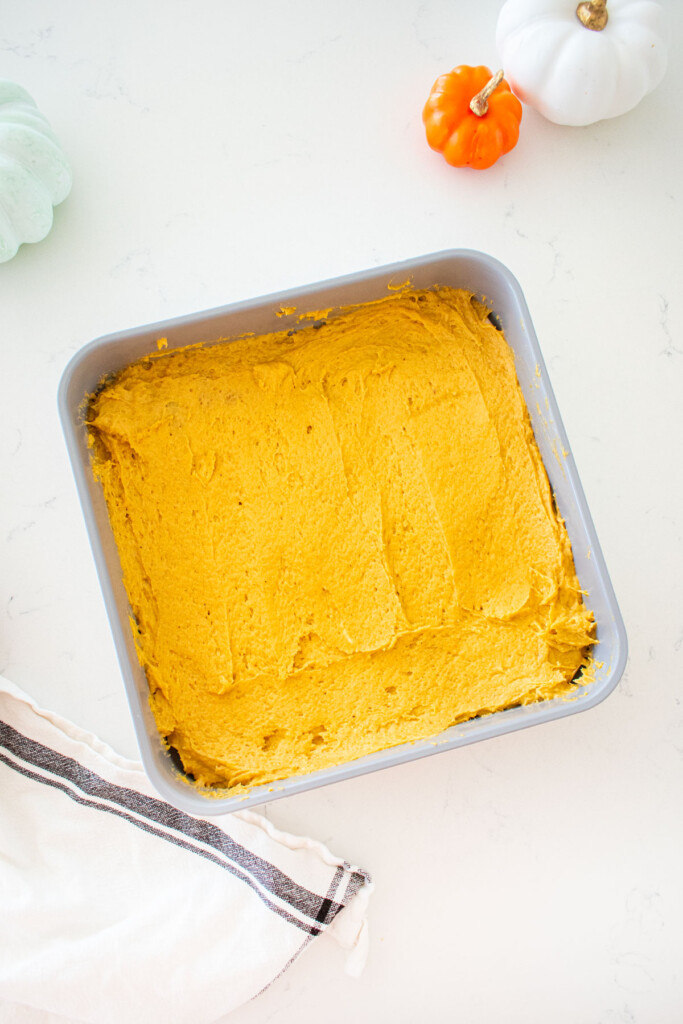 square cake pan with pumpkin spice cake batter spread evenly inside sitting on a marble counter.