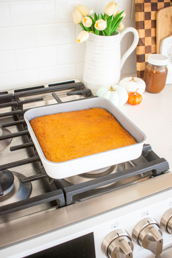 square cake pan with baked pumpkin spice cake cooling on top of an oven.