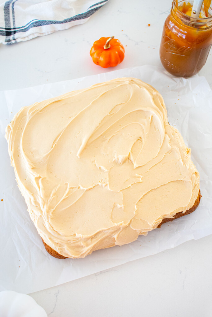 pumpkin spice snack cake with caramel buttercream frosting spread out over the top on a marble counter.