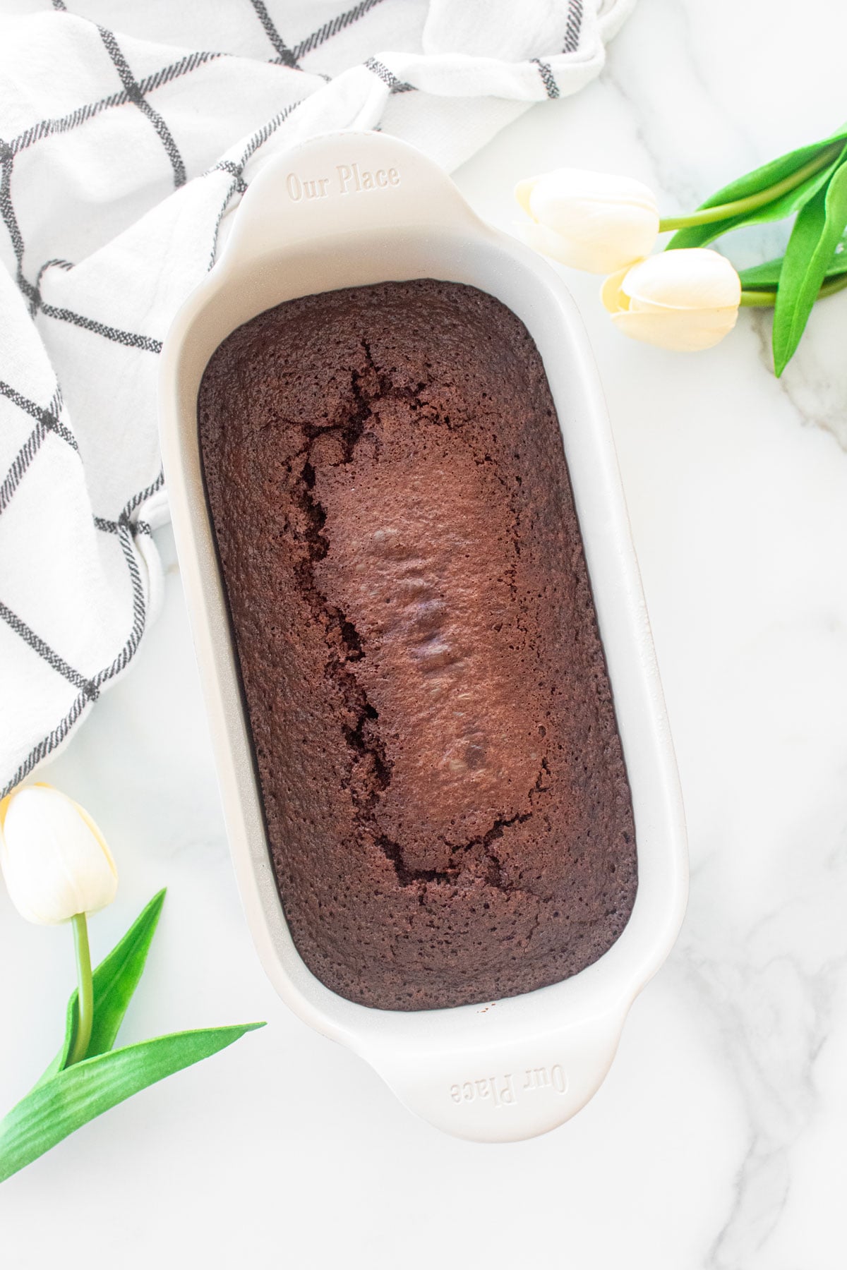 chocolate pound cake in the our place loaf pan on a white marble counter with white tulips.