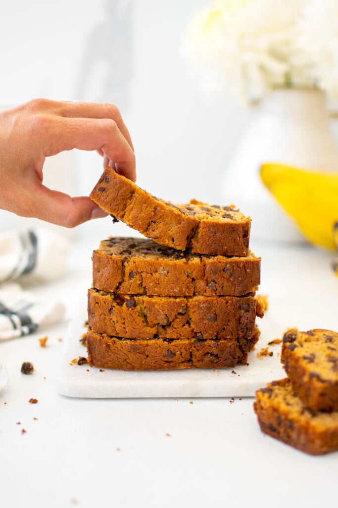 eggless mini chocolate chip banana bread slices stacked, a woman grabbing top slice.