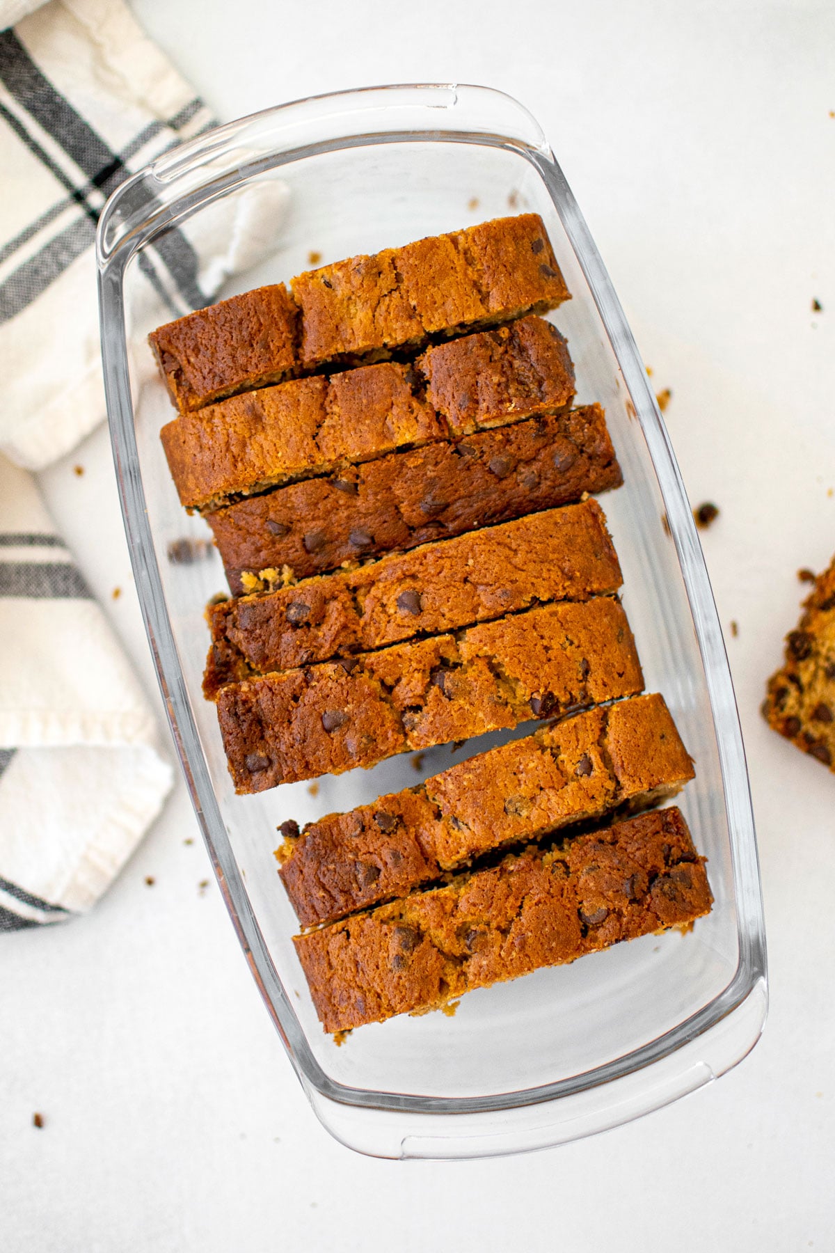 eggless mini chocolate chip banana bread slices in a glass storage container on a white table.