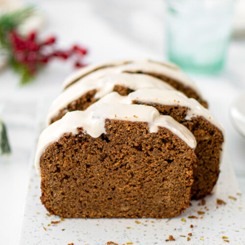 gingerbread banana bread with frosting cut into slices on a marble board.