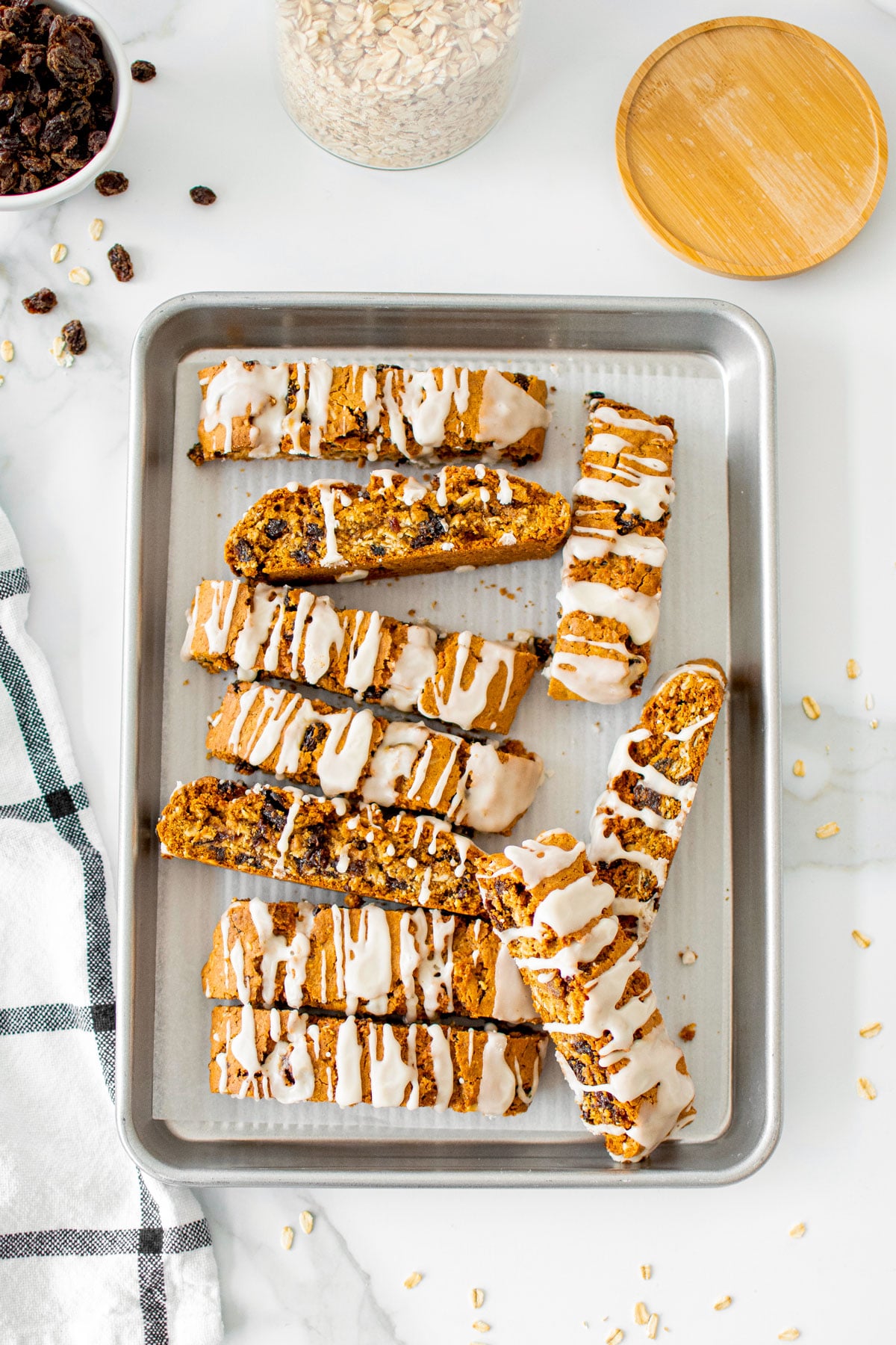 glazed oatmeal raisin biscotti on a baking sheet on a white marble counter.