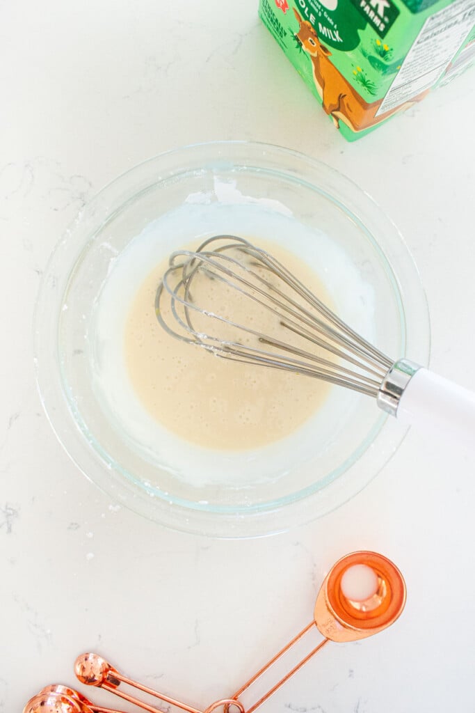 glass mixing bowl with glaze and a whisk on a white marble counter.