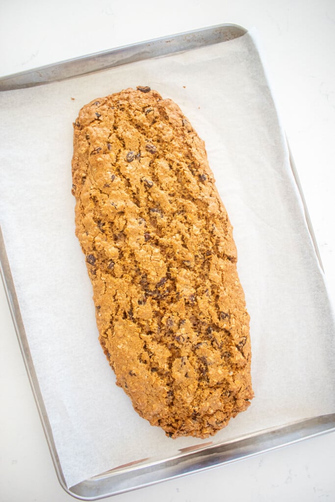 oatmeal raisin biscotti log baked on a baking sheet on a white marble counter.