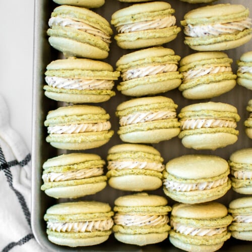 green tea french macarons on a baking sheet on a marble counter.