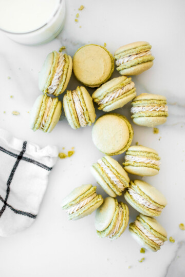 green tea french macarons on a white marble counter with a glass of mik.