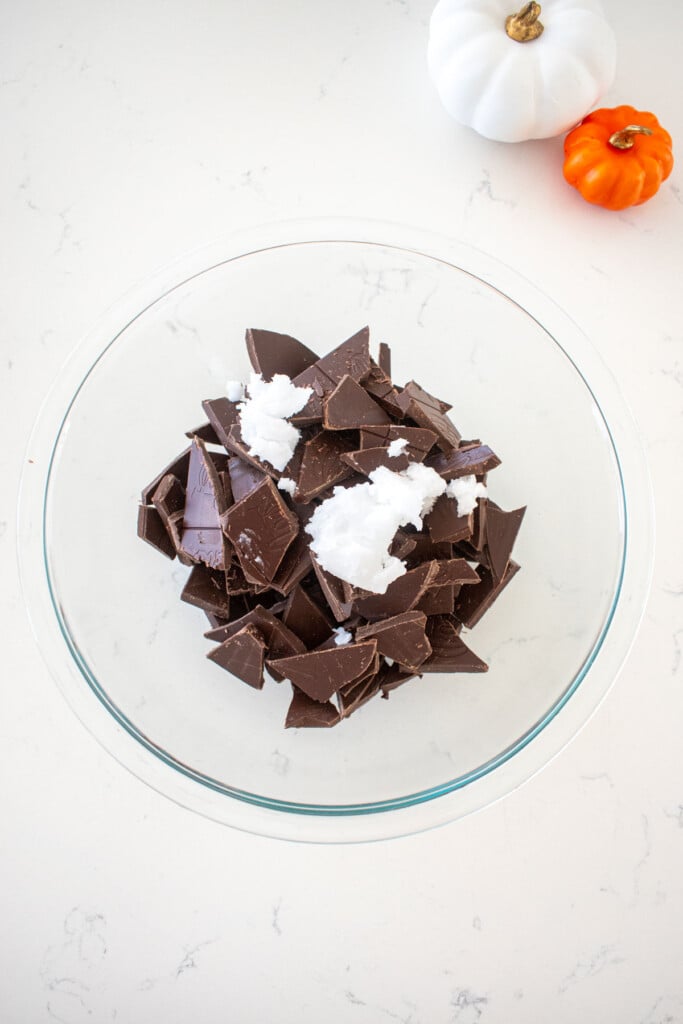glass mixing bowl with milk chocolate chunks and coconut oil on a marble counter.