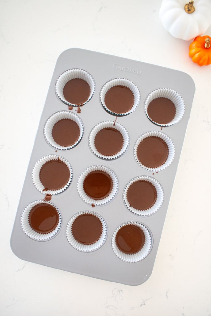 cupcake pan with liners filled one third full of melted milk chocolate on a marble counter.