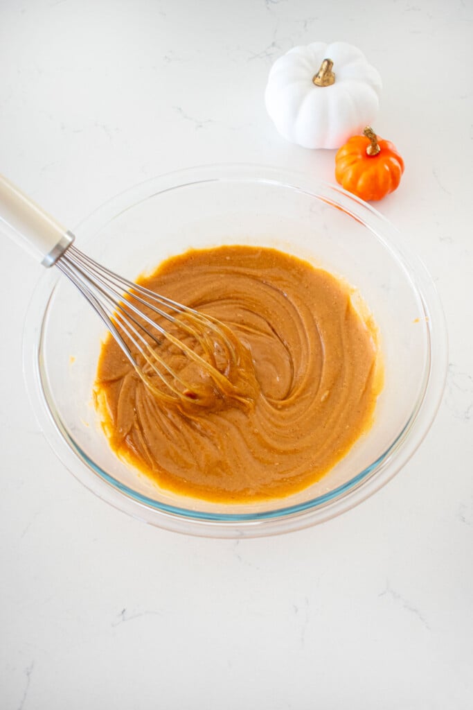 glass mixing bowl with peanut butter filling whisked together on a marble counter with small pumpkins.