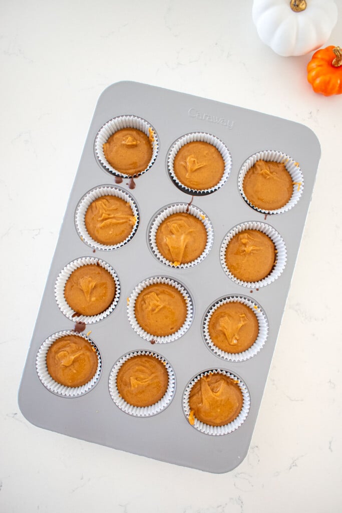 cupcake pan with peanut butter filing filled two thirds full on a marble counter with small pumpkins.
