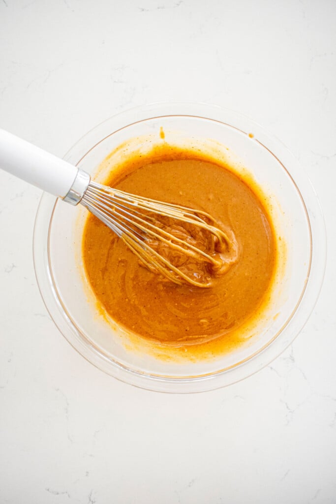 peanut butter filling being mixed in a glass mixing bowl on a white marble counter.
