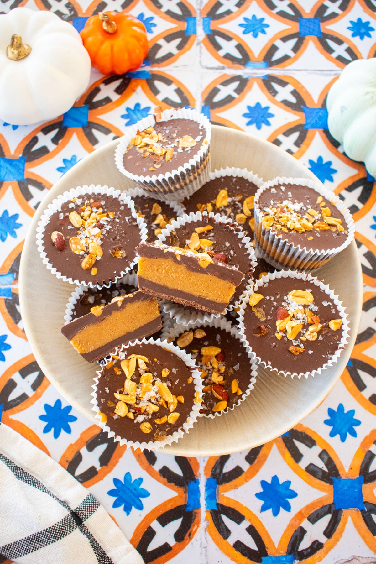 big bowl of healthy chocolate peanut butter cups with one cut in half to reveal peanut butter filling on a tile table with small pumpkins.
